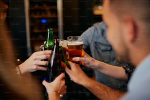 Primer plano de un pequeño grupo de amigos parados en un pub y haciendo un brindis con cerveza.