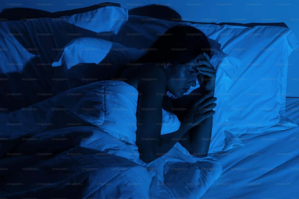 暗い寝室で頭痛と不眠症の若い女性