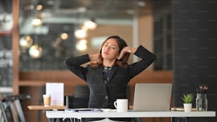 Businesswoman relaxing with hands behind her head at modern office.