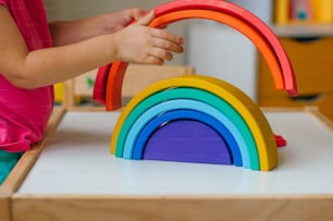 Concepto de juguetes de madera no plásticos. Primer plano de una niña jugando con el arco iris de juguete de madera colorido en la habitación de los niños