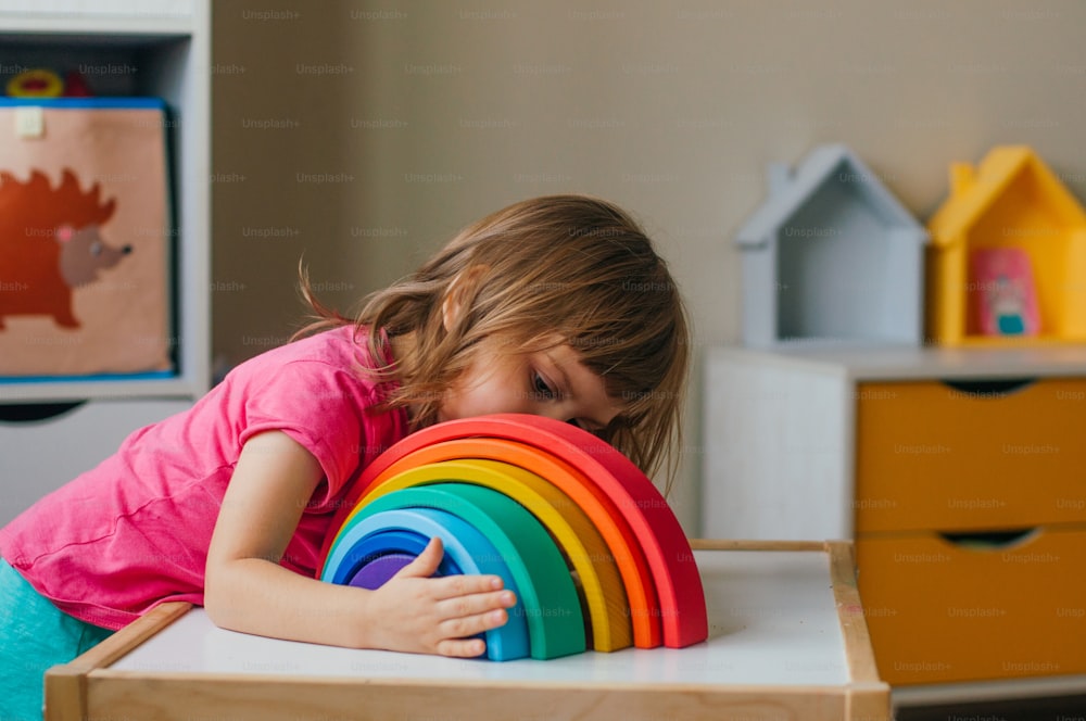 Nicht-Plastik-Holzspielzeug-Konzept. Schönes kleines Mädchen spielt mit buntem Holzspielzeugregenbogen im Kinderzimmer