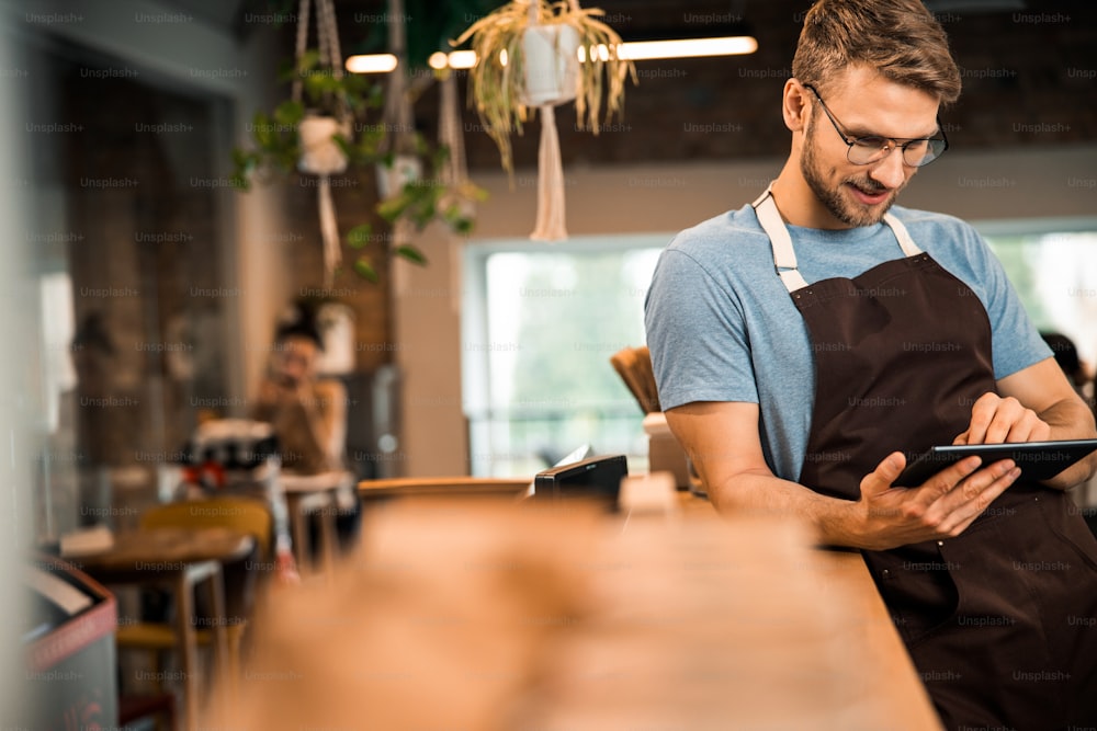 Waist up of male waiter in apron using tablet in coffee house stock photo