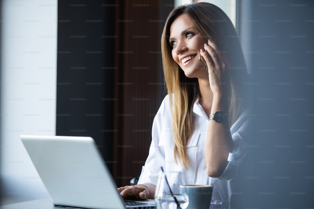 Happy businesswoman sitting at the table and talking on the phone in cafe