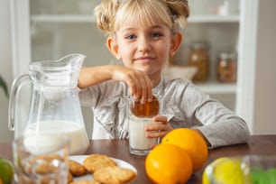 우유와 페이스트리 한 잔을 들고 식탁에 앉아 웃고 있는 사랑스러운 어린 소녀 스톡 사진