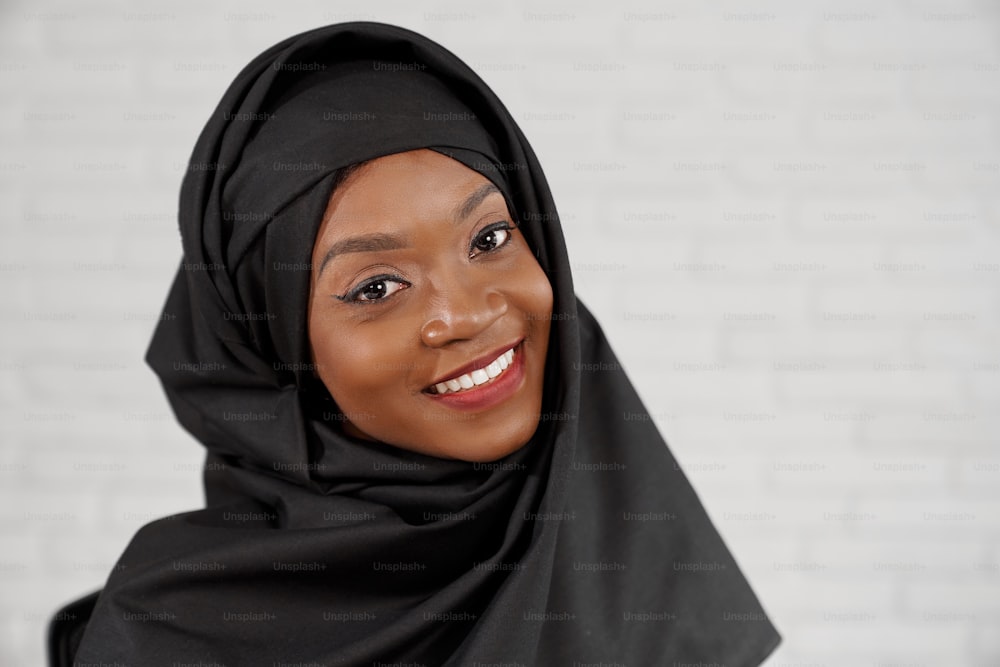 Retrato de bonita, bela mulher muçulmana africana no hijab preto. Mulher elegante com sorriso perfeito posando, sorrindo e olhando para a câmera.