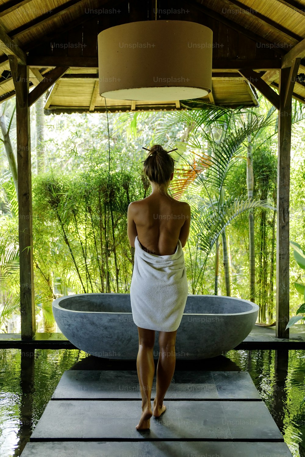 Frau im Open-Air-Badezimmer mit Steinbadewanne im balinesischen Stil
