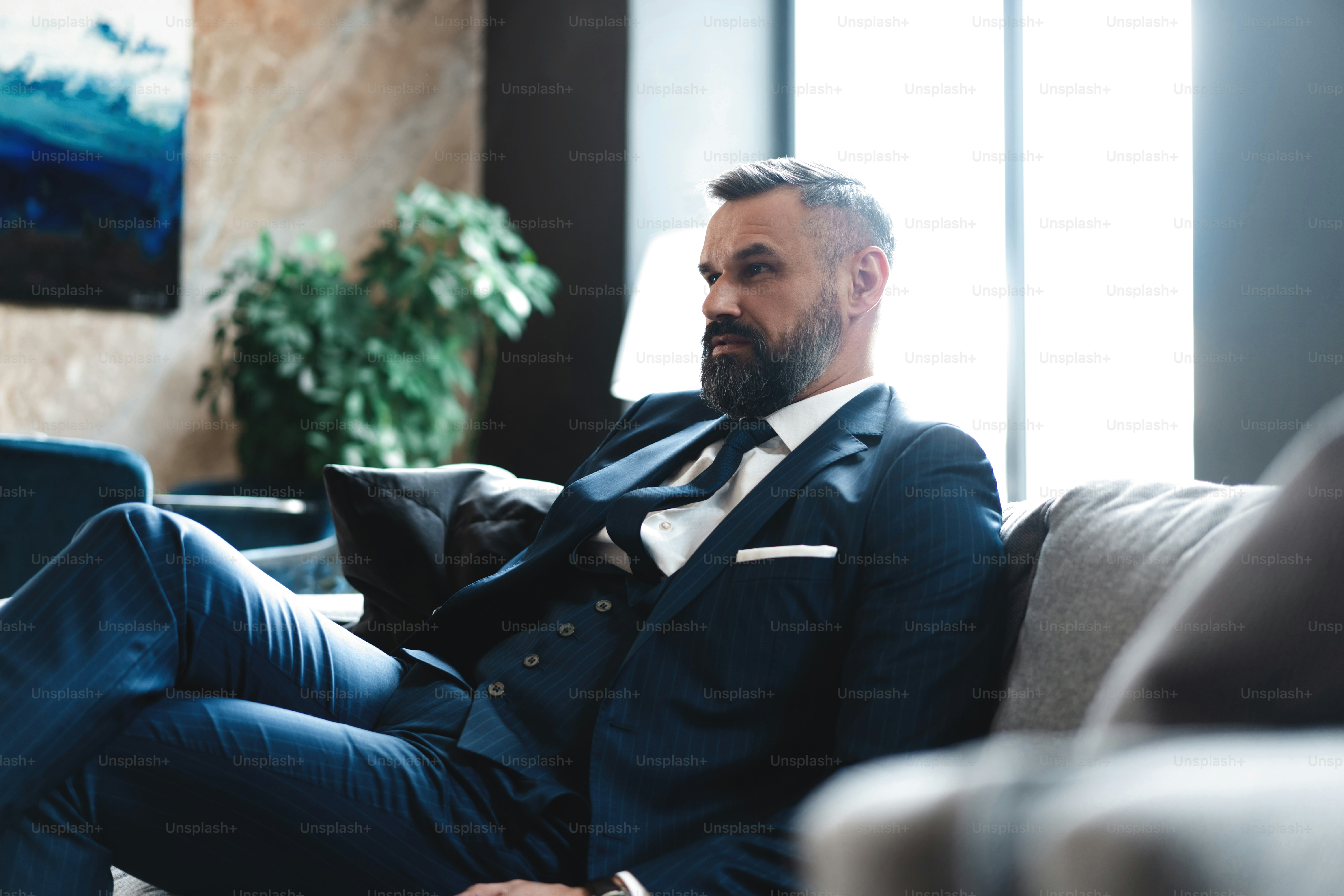 Confident and concentrated. Thoughtful handsome businessman thinking while sitting in his modern office about business concept while sitting on sofa