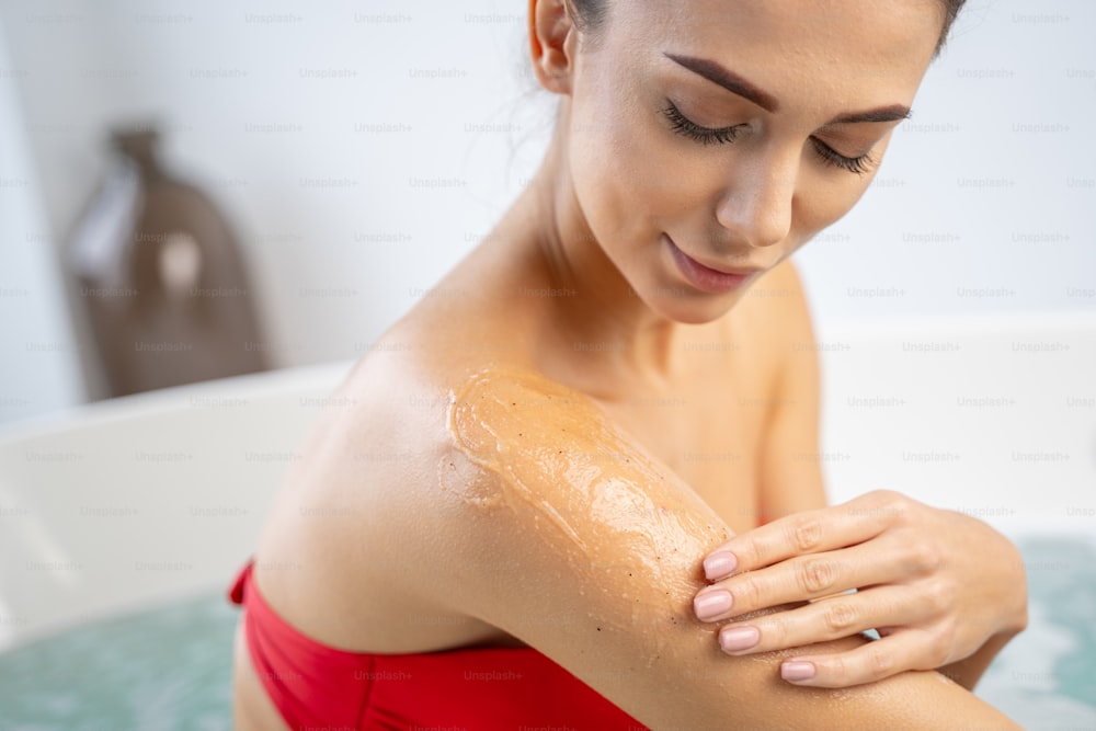Girl applying a layer of body gel scrub on her skin