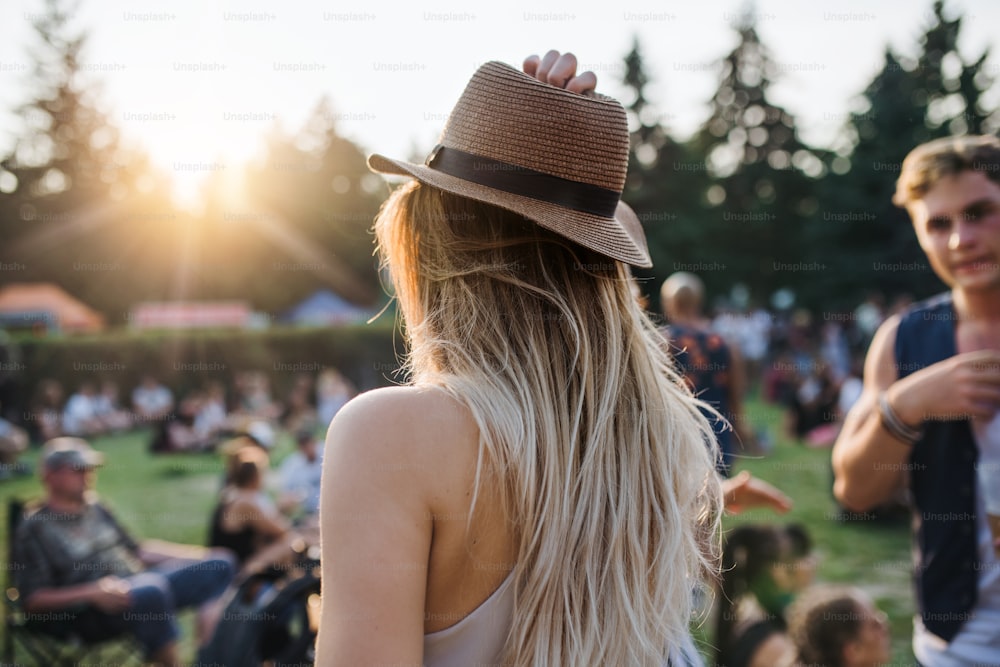 A rear view of young woman with hat standing at summer festival or camping holiday.