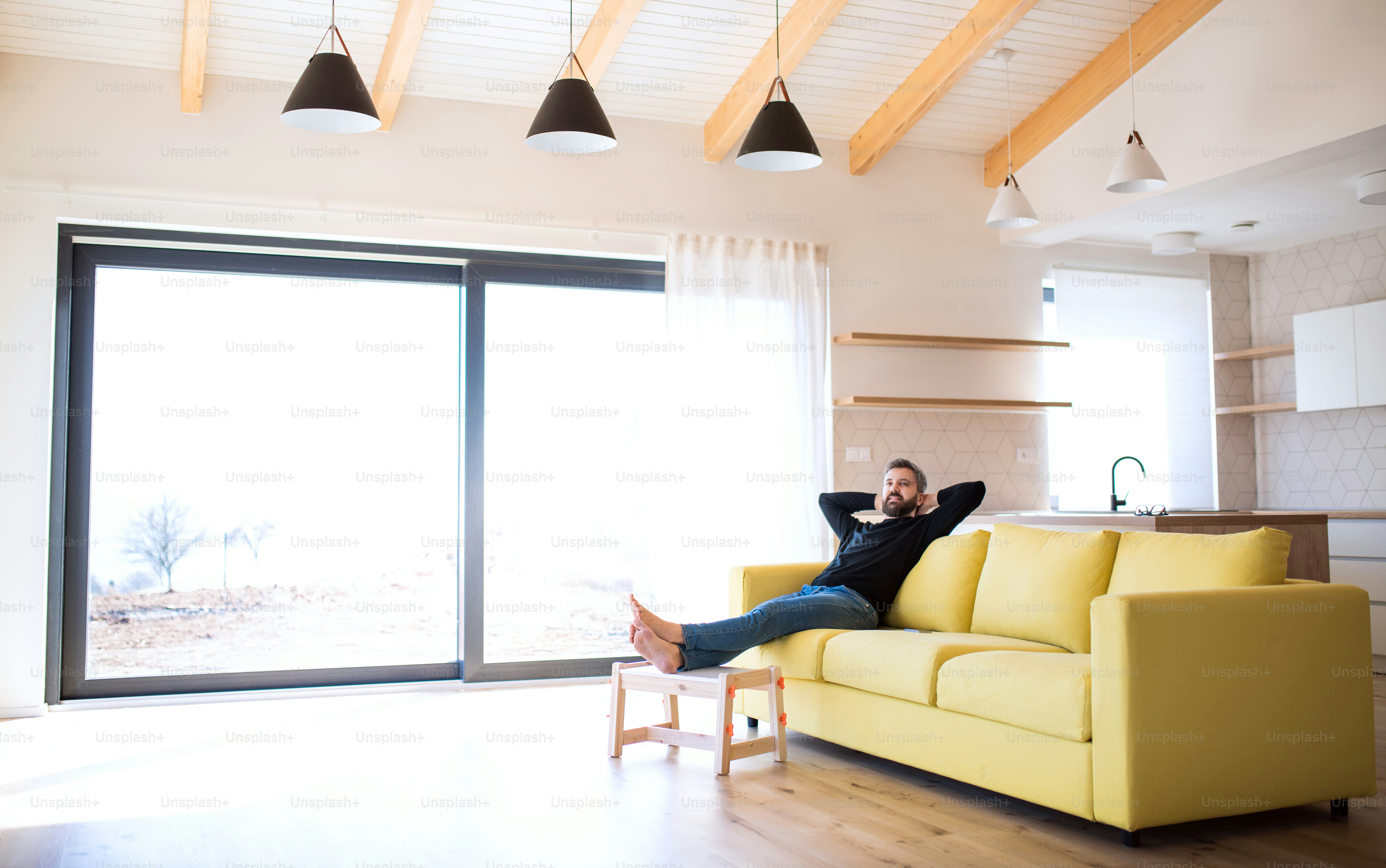 Cheerful mature man sitting on sofa in unfurnished house, moving in new home concept.