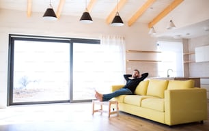 Hombre maduro alegre sentado en el sofá en una casa sin amueblar, moviéndose en un nuevo concepto de hogar.