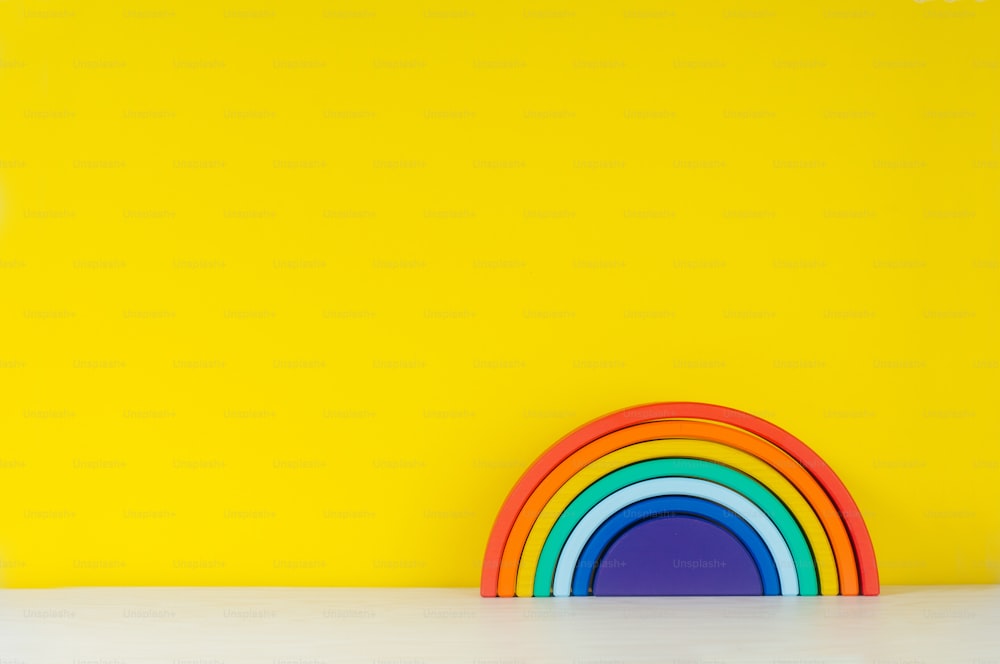 Wooden toy rainbow on the shelf on yellow background with blank text for text.