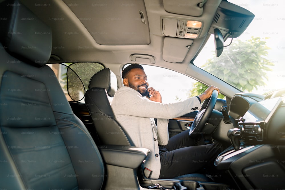Hombre de negocios guapo negro que conduce el automóvil hablando en un teléfono inteligente