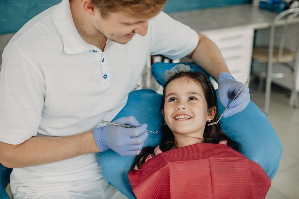 Belle petite fille assise dans une chaise de stomatologie regardant son dentiste souriant avant de faire une chirurgie dentaire