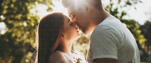 Side view portrait of a amazing caucasian couple kissing against golden hour light embracing while dating outside.