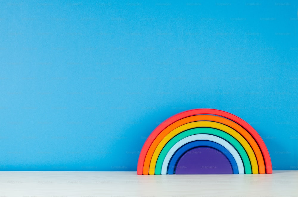 青い背景に子供部屋の棚にある木製のおもちゃの虹とテキストの空白のテキスト。