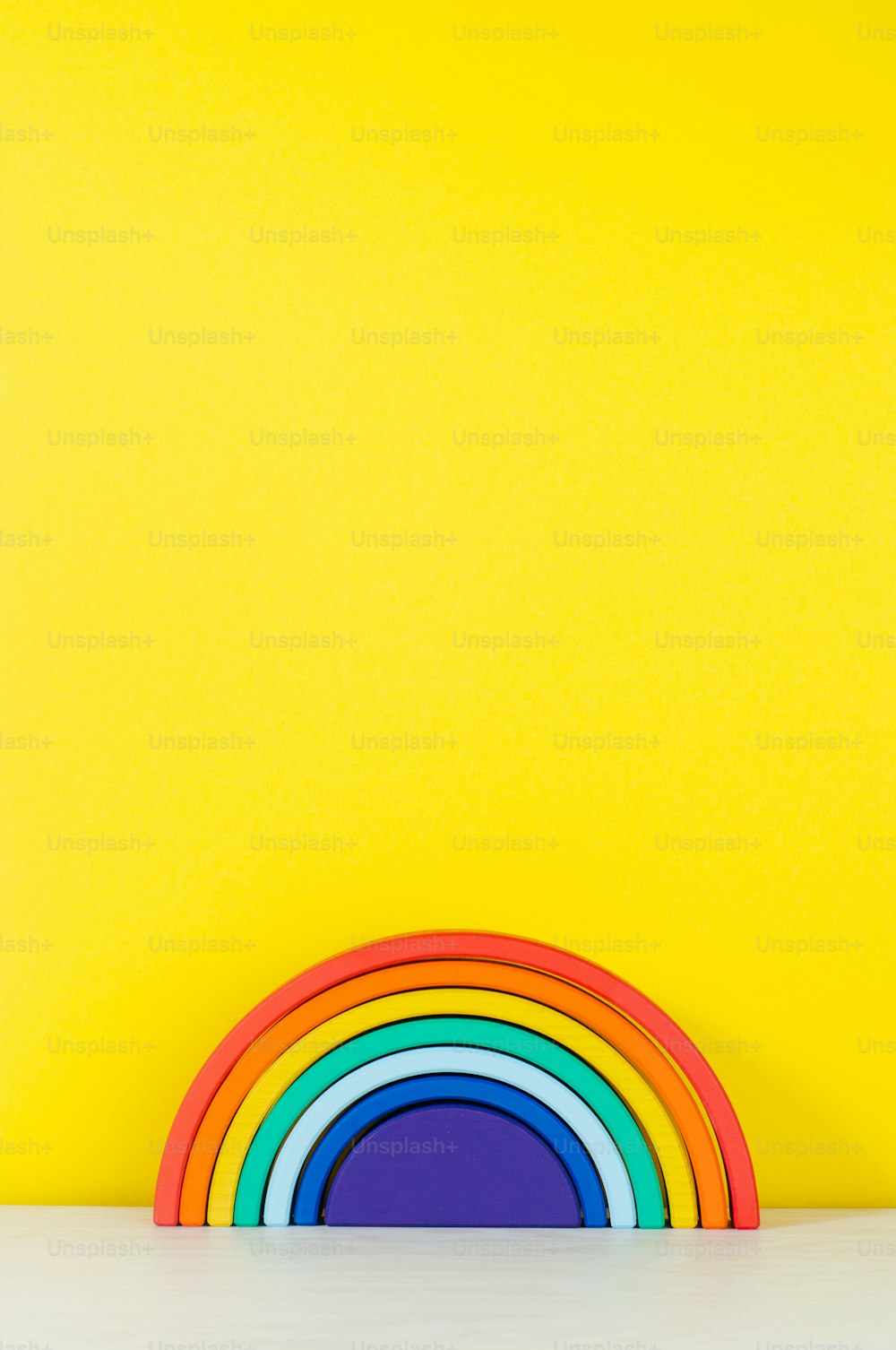 黄色の背景に子供部屋の棚にある木製のおもちゃの虹とテキストの空白のテキスト。