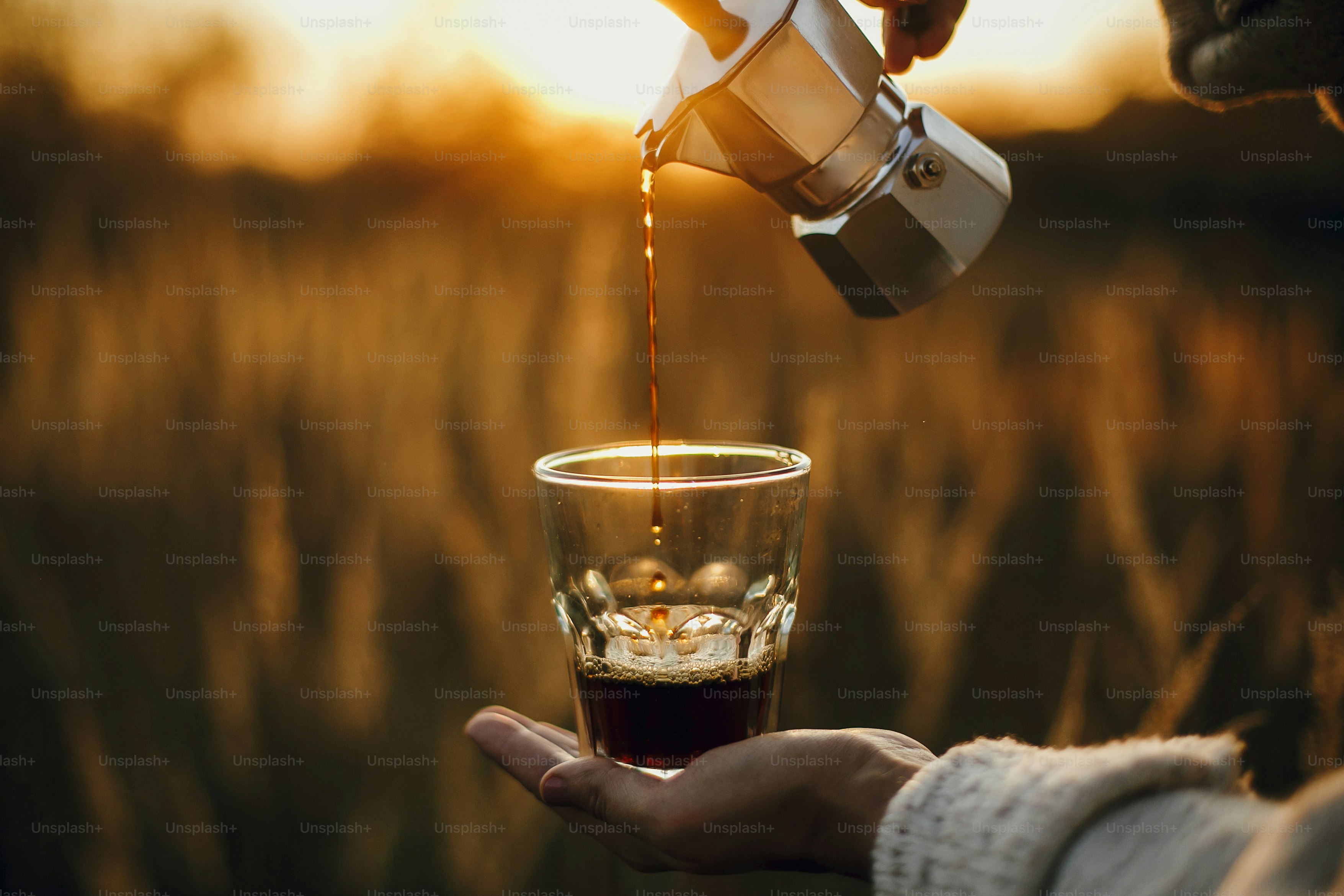 Hipster pouring fresh hot coffee from geyser coffee maker into glass cup in sunny warm light in rural countryside herbs. Atmospheric tranquil moment. Alternative coffee brewing in travel