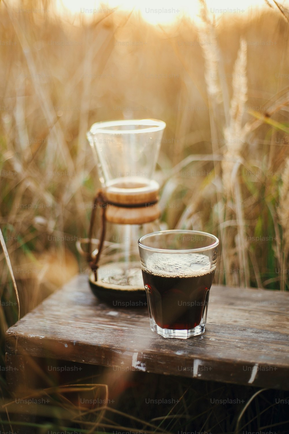 Préparation alternative du café à l’extérieur en voyage. Café chaud dans une tasse en verre et une fiole en verre sur fond dans une lumière chaude et ensoleillée dans les herbes rurales. Moment tranquille rustique atmosphérique. Image verticale