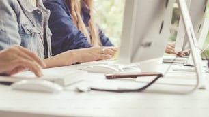 Primer plano de la mano de la mujer de negocios escribiendo a mano y trabajando en la computadora de escritorio en el escritorio de la oficina. Comunicación empresarial y concepto de lugar de trabajo.