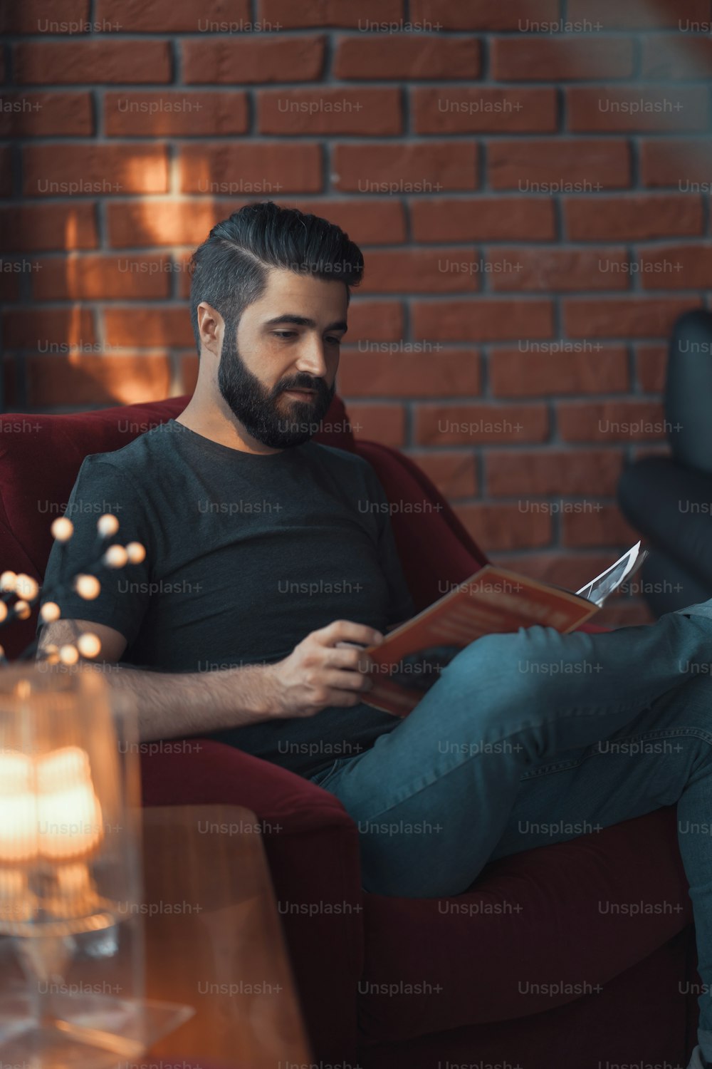 Porträt gutaussehender bärtiger Mann in Freizeitkleidung. Mann sitzt im roten Stuhl modernes Loft-Studio, liest Comics und entspannt