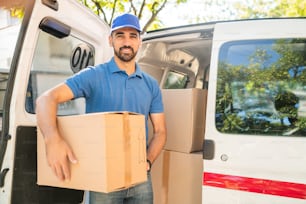 Portrait of a delivery man unloading cardboard boxes from van. Delivery service and shipping concept.