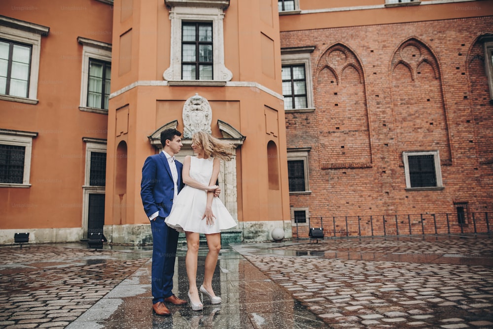 Stylish couple dancing in european city street on background of old architecture. Fashionable man and woman in love dancing with passion in city. Traveling together in Europe