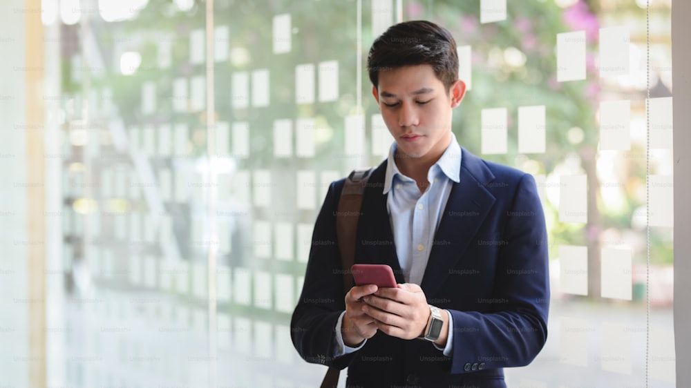 Cropped shot of young professional businessman texting on smartphone while standing in office room