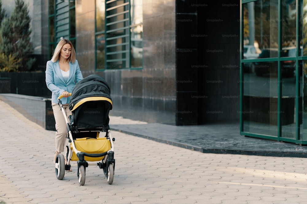 Portrait of a successful business woman in blue suit with baby. Business woman pushing baby stroller