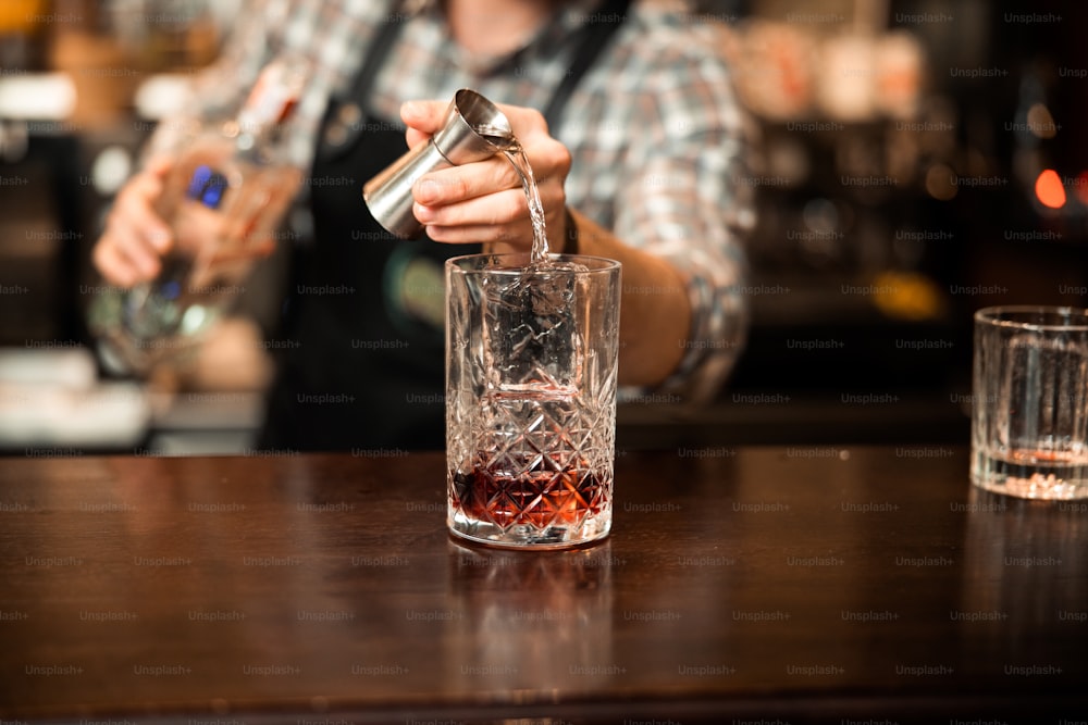 Beschnittenes Foto des Barkeepers, der frisches alkoholisches Getränk in die Gläser gießt Stockfoto
