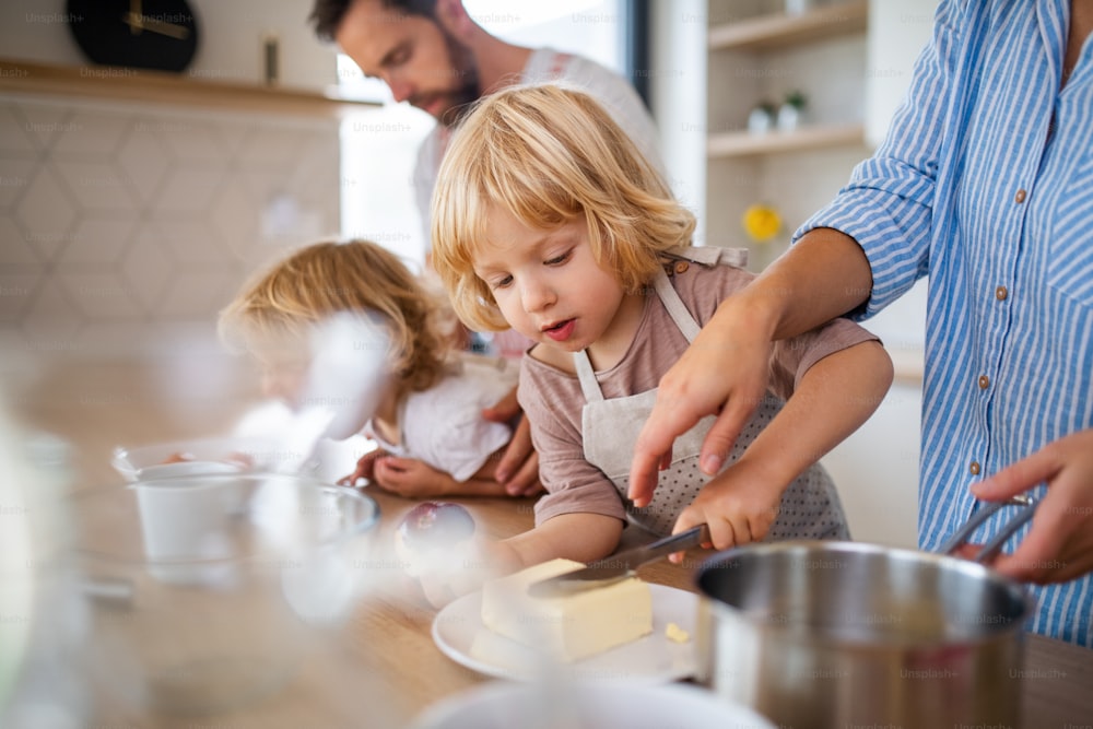 A young family with two small children indoors in kitchen, preparing food.