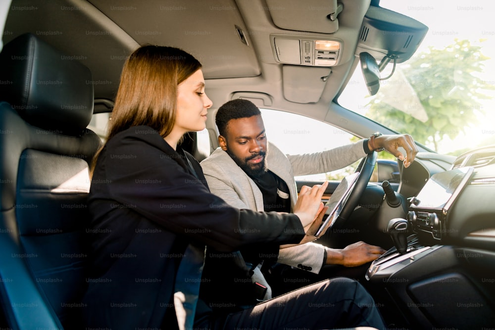 business automobilistico, vendita di auto, navigazione e concetto di persone - primo piano di coppia multietnica seduta in auto con tablet computer e guardando lo schermo.