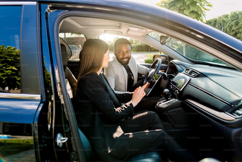 young beautiful couple, business partners, multiethnical man and woman, using tablet in the car business travel.