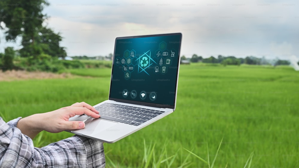 Close-up image of young modern farmer controlling the automatic water supply system by using laptop for cultivated rice in field. Agricultural technology concept.