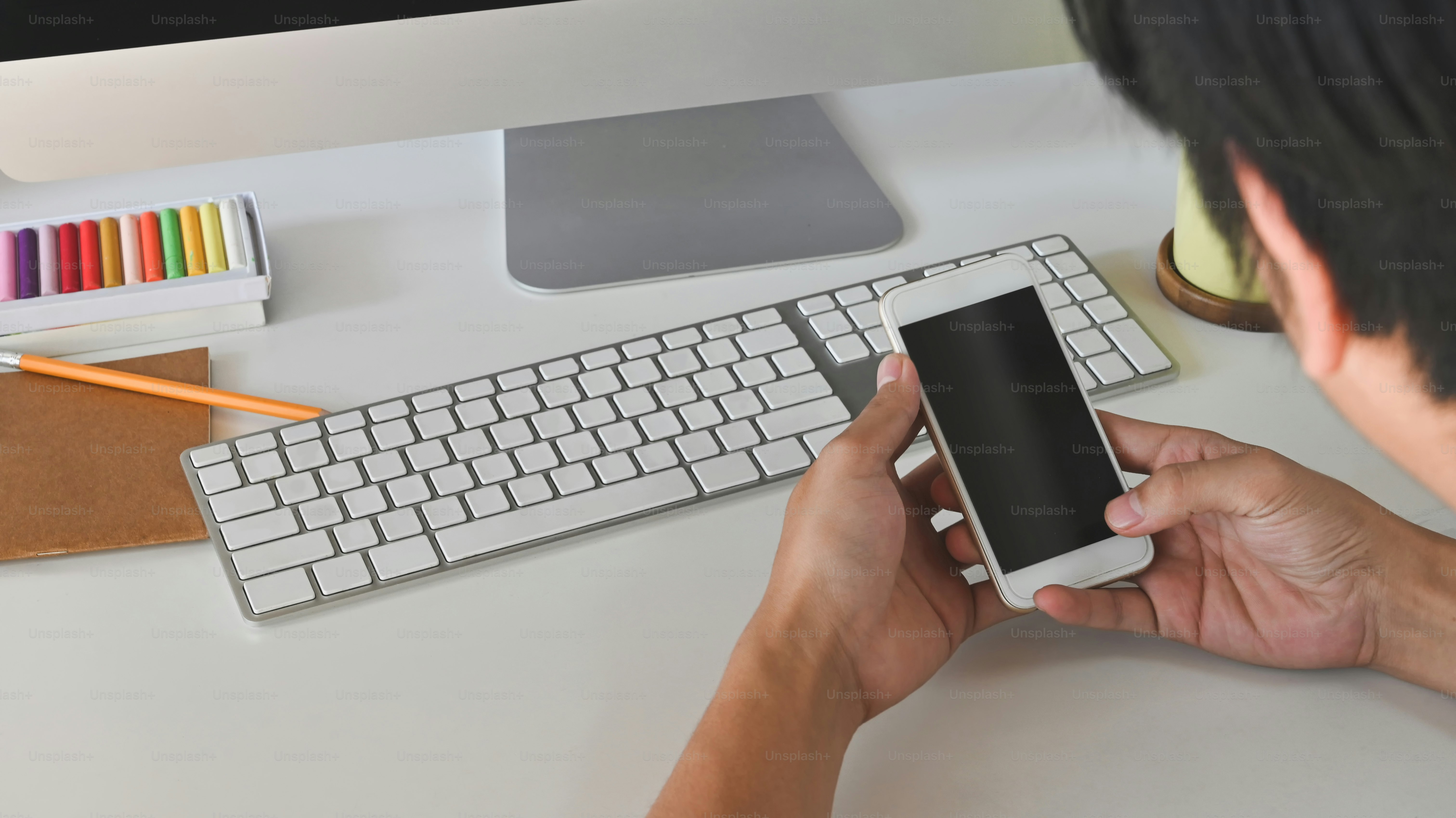 Cropped shot of modern working desk and hand while holding a black blank screen smartphone.