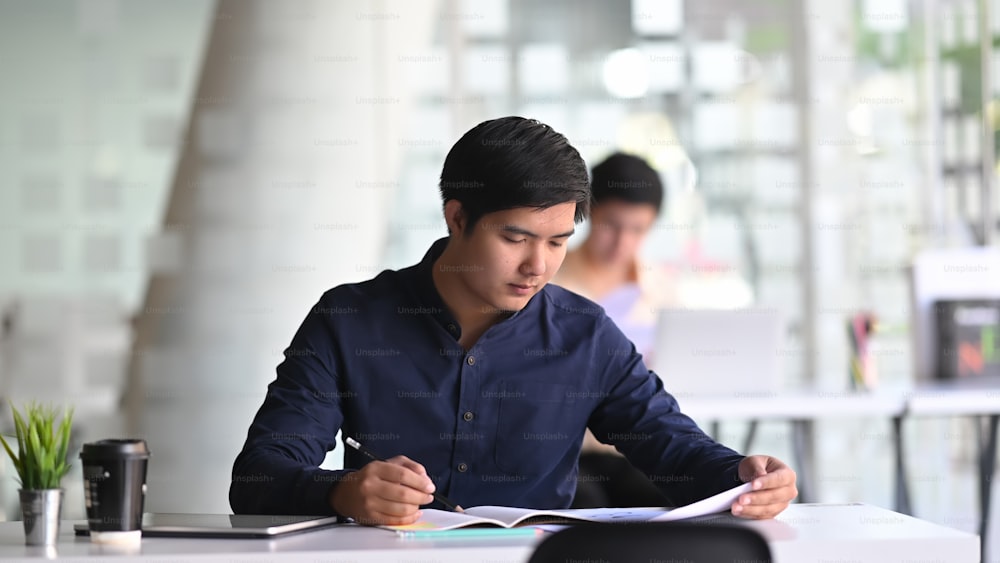 Foto eines jungen Geschäftsmannes schreibt auf das Geschäftsdokument am modernen Schreibtisch vor seinem Kollegen.