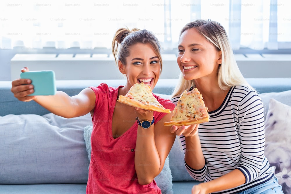 피자를 먹고 셀카를 위해 웃는 친구들. 그들은 피자를 공유하고 모바일 스마트 폰에서 셀카 사진을 만들고 있습니다. 그들은 집에서 파티를하고 피자를 먹고 재미있게 놀고 있습니다.