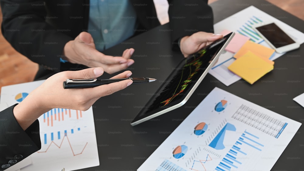 ビジネスマンが金融やビジネスの成長について議論/分析する様子を、画面上にローソク足チャートを載せたタブレットを使って撮影したショット。