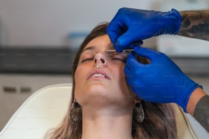 Mann zeigt einen Piercing-Prozess mit sterilen medizinischen Geräten und Latexhandschuhen. Markieren der Piercingstelle. Piercing-Verfahren. Piercing . Schöne Frau, die ihr Gesicht durchbohrt bekommt