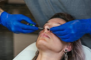 Portrait of a woman getting her nose pierced. Man showing a process of piercing nose with steril neadle and latex gloves. Nostril Piercing Procedure. Beautiful woman getting her nose pierced