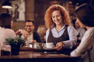 バーで働いている間、女性客にコーヒーを飲ませる若い幸せなウェイトレス。