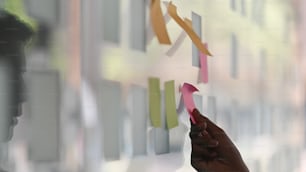 Plan latéral d’un jeune homme d’affaires tandis qu’un post-it sur un mur de verre. Tableau de calendrier de rappel de papier de note autocollante. Concept de remue-méninges.