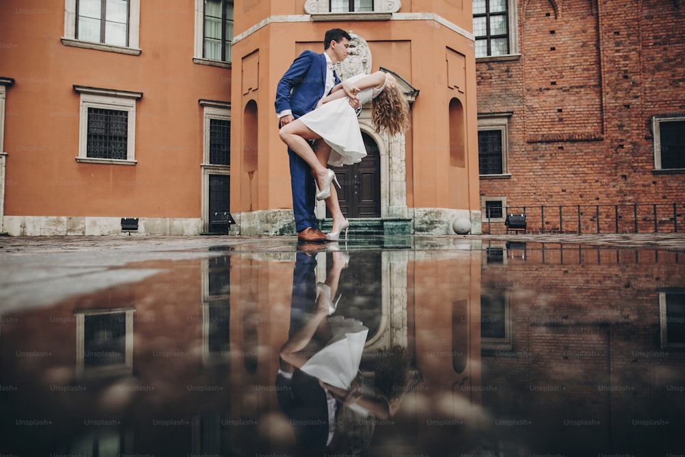 Coppia elegante che balla nella strada della città europea sullo sfondo della vecchia architettura e del riflesso nell'acqua. Uomo e donna alla moda innamorati che ballano. Viaggiare insieme in Europa