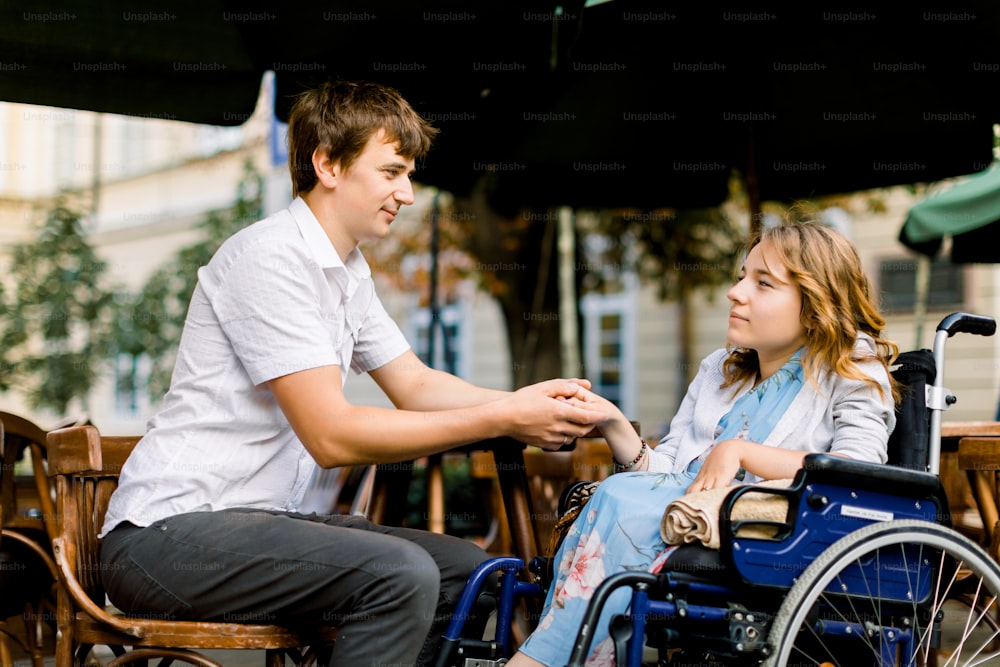 Pretty young woman on a wheelchair enjoying some good company on a date with her handsome man at a cafe outdoors in the city.