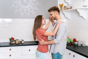 Side view of happy young adult husband and wife making rejoiced faces, smiling wide, dancing on kitchen together, spending weekend at home with modern interior