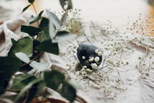 Happy Easter. Stylish easter egg in rustic nest with feathers on wooden table. Natural dyed blue easter egg with eucalyptus branch, white spring flowers on rural textile background.