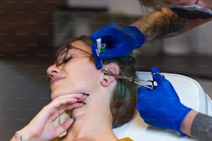 Portrait of a woman getting her ear pierced. Man showing a process of piercing ear with sterile neadle and latex gloves. Ear Piercing Procedure. Body Piercing . Beautiful woman getting her ear pierced