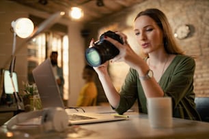 オフィスで遅くまで仕事をしながらカメラで写真を見ている女性写真家のローアングルビュー。