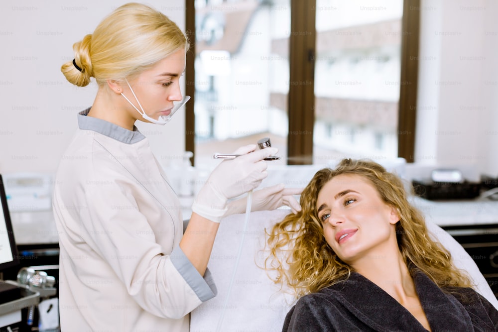 Junge Kosmetikerin macht professionelle Gesichtsfeuchtigkeit für eine hübsche Frau in der Beauty-Spa-Klinik, Nahaufnahme.