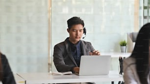 Photo of young smart operator man with headsets while working in a call center surrounded by colleague.